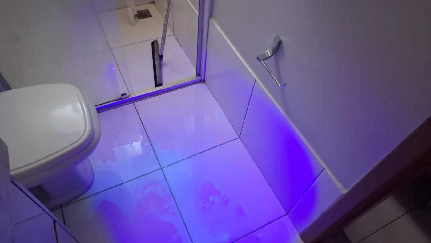 Piso de banheiro sob luz ultravioleta, com manchas fluorescentes fora do box